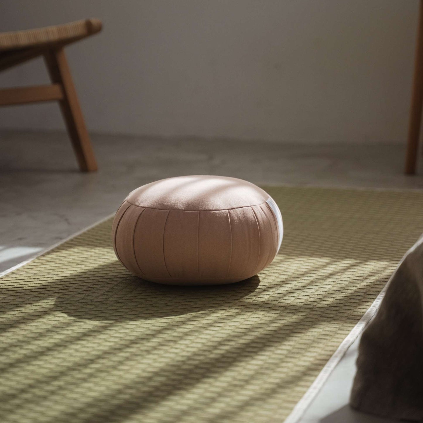 Smoky rose zafu meditation cushion sitting on a tatami mat in a peaceful room with sunlight shadows.