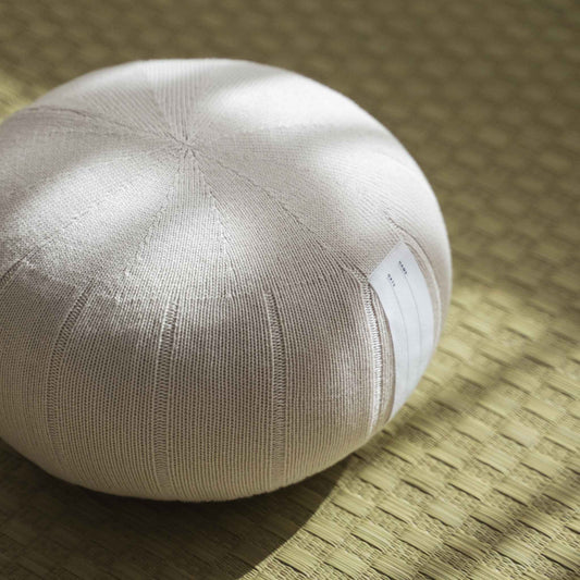 Close up of white grey zafu meditation cushion showing organic cotton knit texture on a tatami mat.