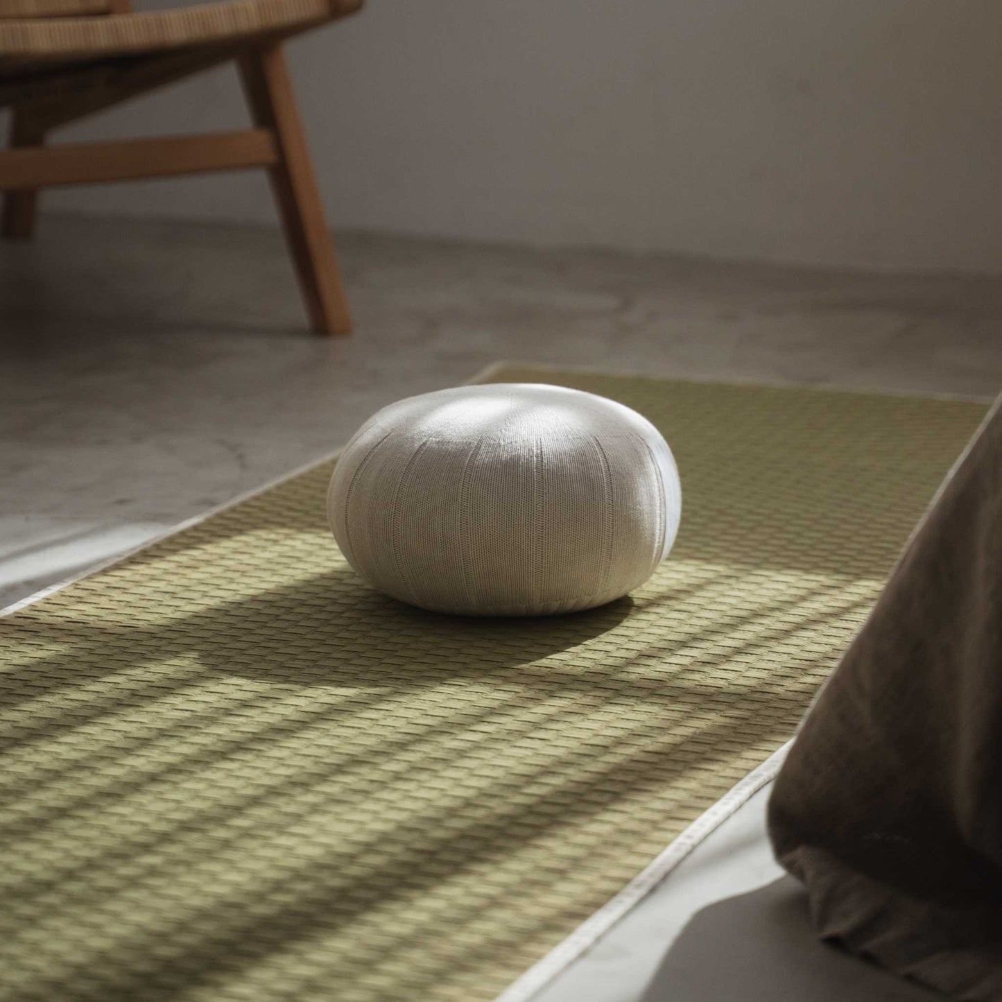 White gray zafu meditation cushion resting on a green tatami mat in a peaceful sunlit zen space.