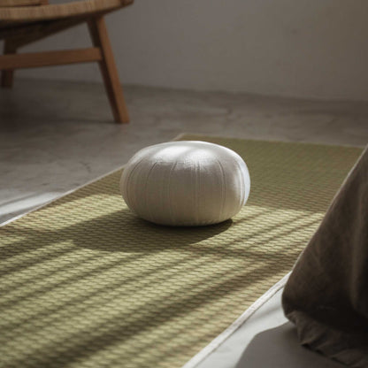 White gray zafu meditation cushion resting on a green tatami mat in a peaceful sunlit zen space.