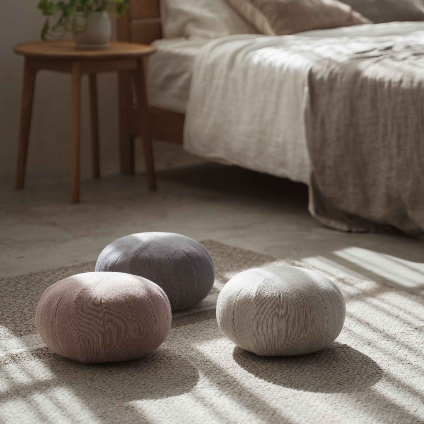 Three round zafu meditation cushions placed on the floor near a bed with linen sheets in a cozy room.