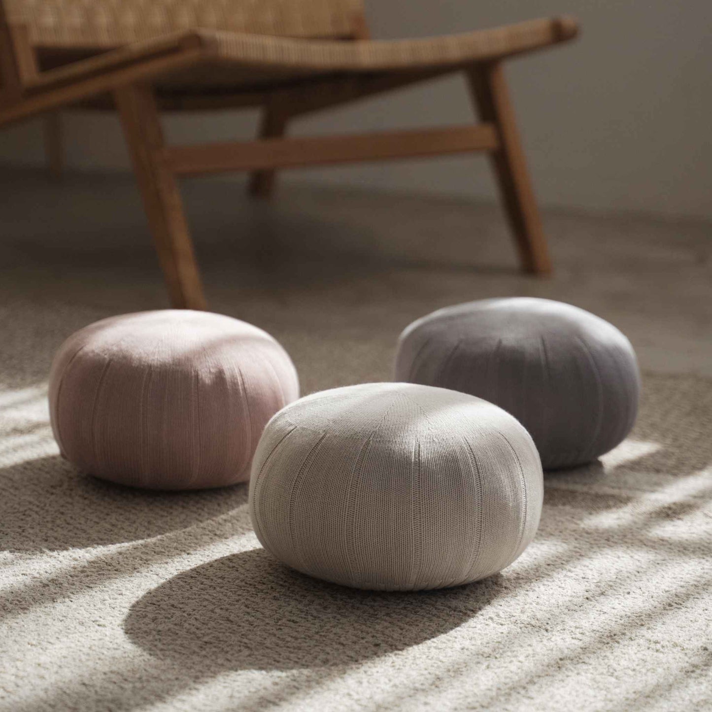 Trio of round japanese zafu meditation cushions sitting on a carpet in a sunlit room near a wooden chair.